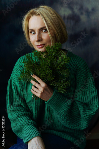 Portrait of a beautiful woman with a green sweater with fir branches in her hands.