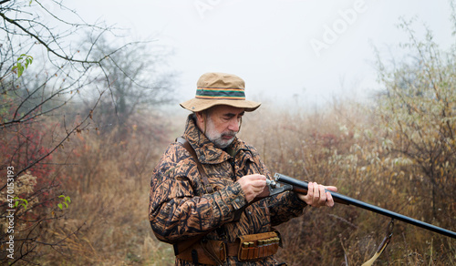hunter man with a gray beard in hunter suit load cartridges in a double-barreled rifle