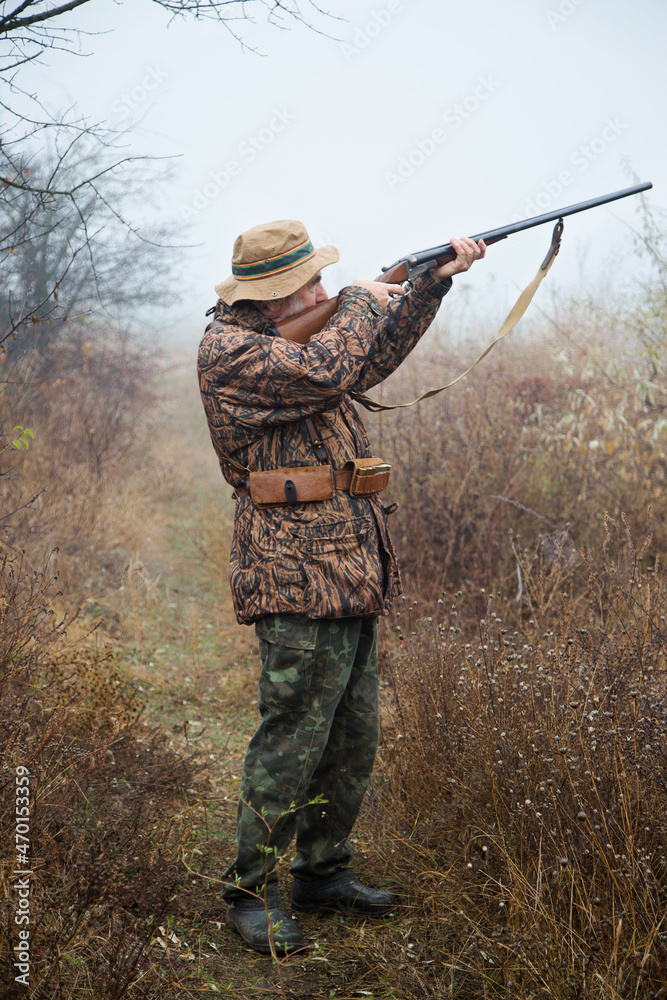 Fototapeta premium hunter man with a gray beard in hunter suit makes aiming wiring with a double-barreled rifle 