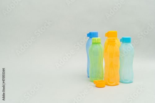 Plastic Tupperware Bottles. A stack of colour water bottles, blue, orange and green on a grey background, one bottle cap off.