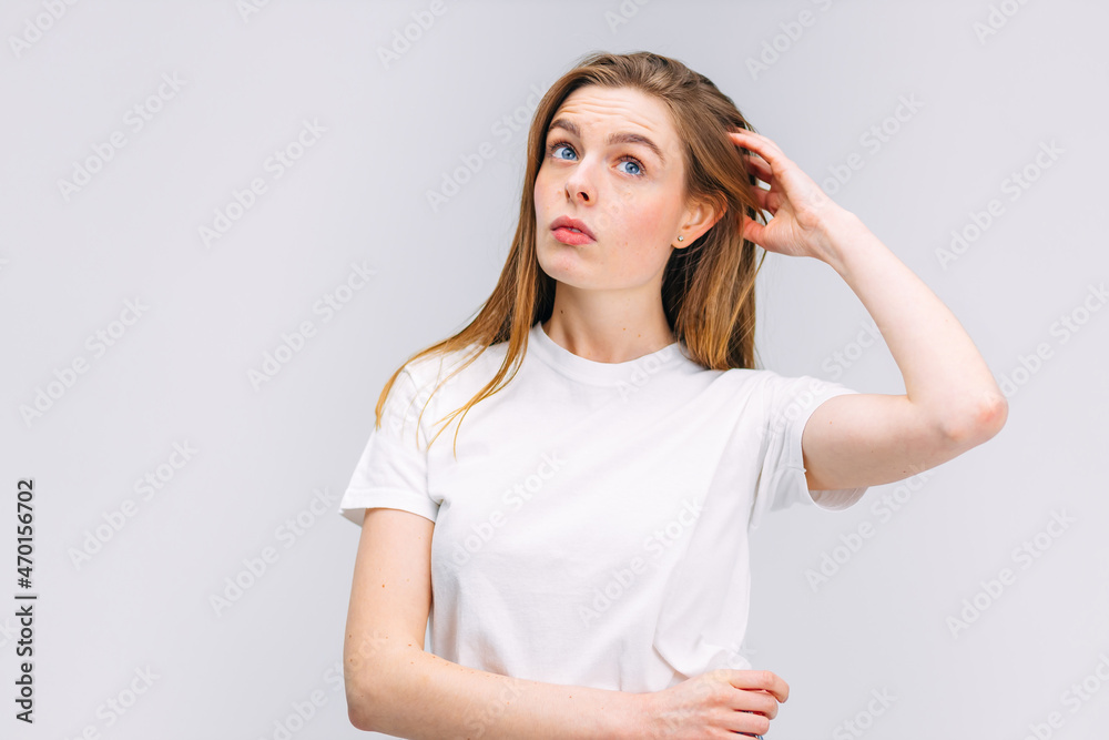 Girl in white shirt doubts scratching her head on isolated gray background Girl in white shirt doubts scratching her head on isolated gray background