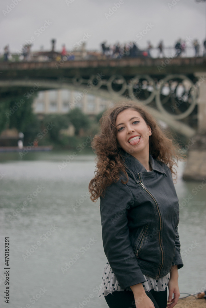 Tourist girl smiling happily to camera outdoors with Triana Bridge in the background.