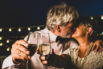 Old caucasian couple kissing each other while toasting champagne glasses celebrating new year party. Loving husband and wife kissing each other while partying with white wine glasses in hands