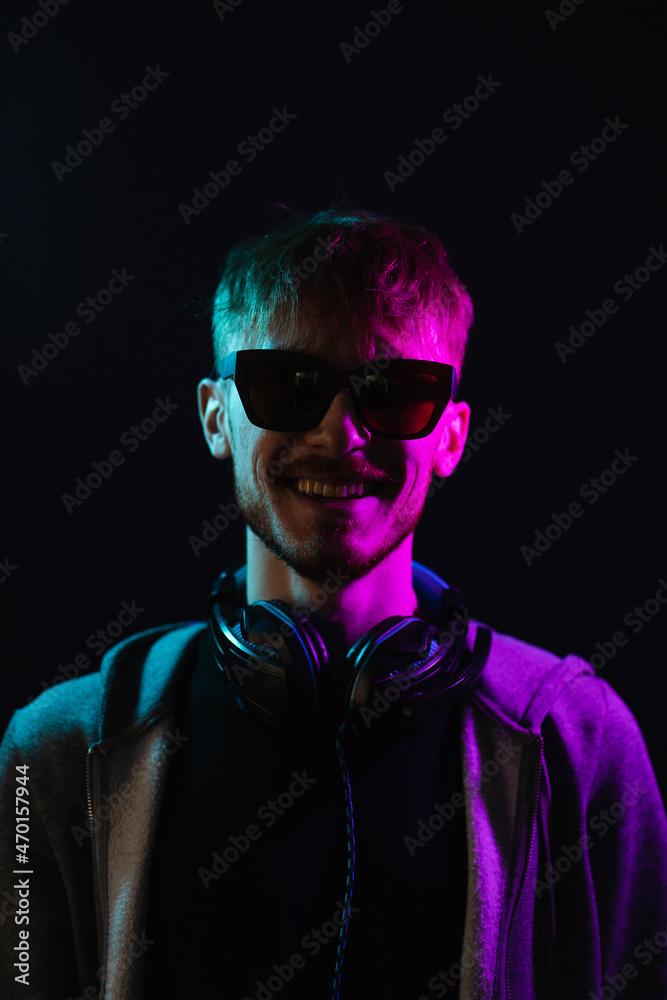 Neon portrait of a bearded man wearing headphones on the neck, wearing parka and sunglasses. Hacker portrait