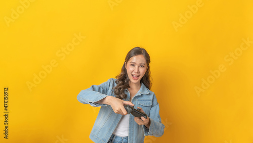 Game Online. asian pretty woman gamer in denim Jacket playing game online exciting with joystick controller on copy space yellow background, pro gamer, entertainment, internet technology concept © Vittaya_25
