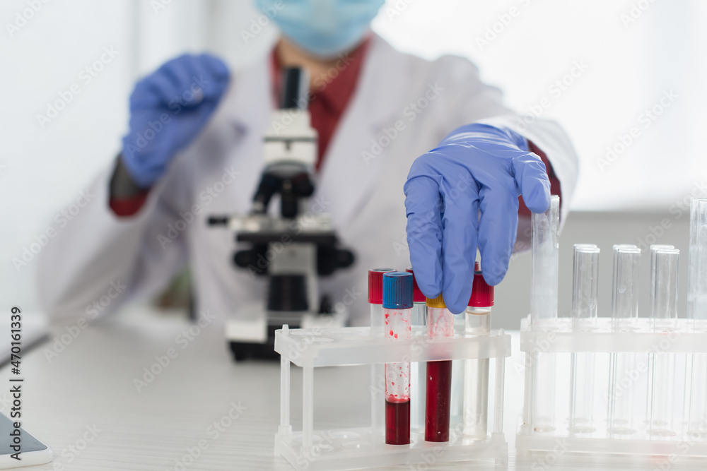cropped view of scientist in latex gloves and medical mask reaching test tubes near blurred microscope. cropped view of scientist in latex gloves and medical mask reaching test tubes near blurred microscope.