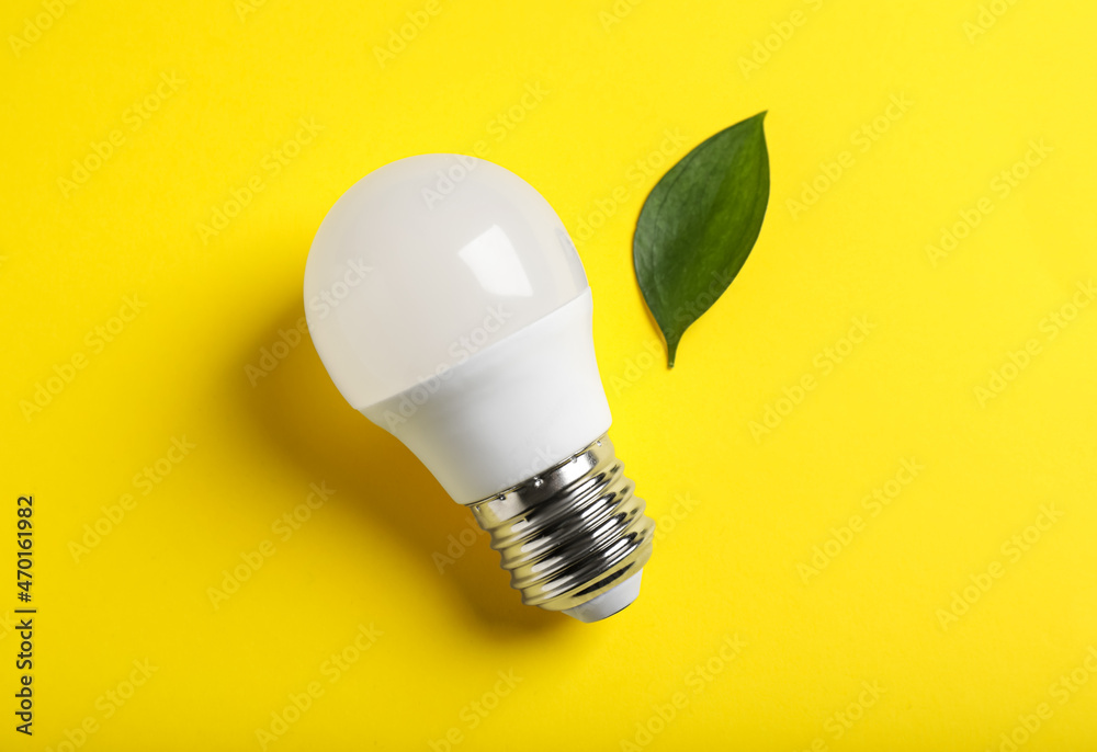 Light bulb and green leaf on yellow background, flat lay Light bulb and green leaf on yellow background, flat lay