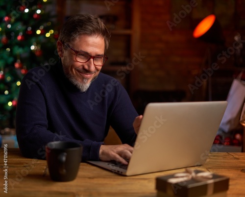 Bearded man using laptop computer at home. Portrait of middle age, mid adult man in 50s shopping online for Christmas, browsing web.