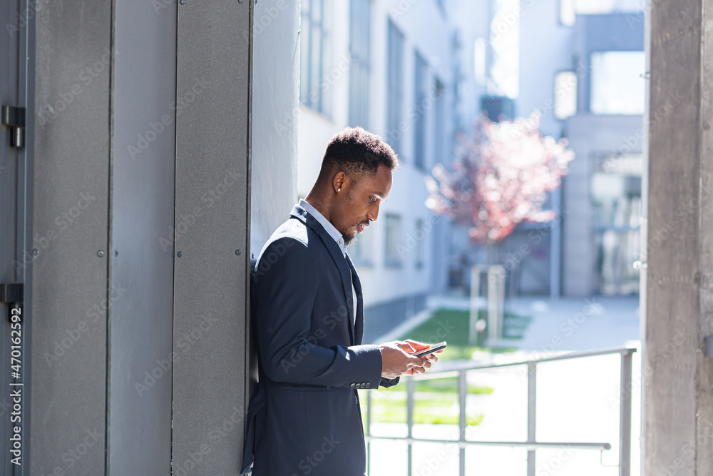Successful and happy african american businessman near office holding mobile phone smiles and rejoices reads news and writes Successful and happy african american businessman near office holding mobile phone smiles and rejoices reads news and writes