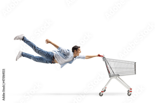 Full length shot of a casual guy man flying and holding an empty shopping cart photo