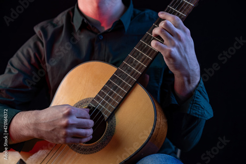 The guy in the dark shirt is plucking the strings of a six-string guitar