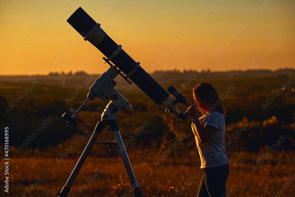 Silhouette of a woman, astronomical telescope and countryside.