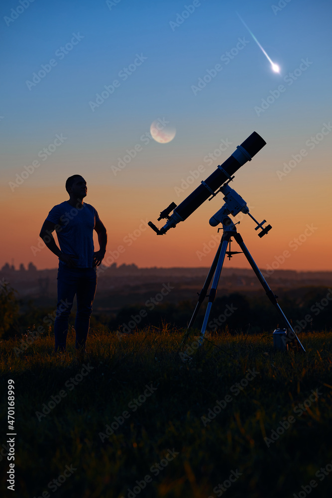 Silhouette of a man, astronomical telescope, countryside, lunar eclipse and meteor shower.