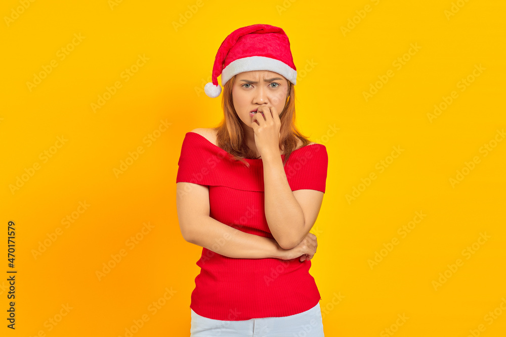 Young Asian woman wearing Christmas hat looking stressed and nervous with hand on mouth biting nails Young Asian woman wearing Christmas hat looking stressed and nervous with hand on mouth biting nails