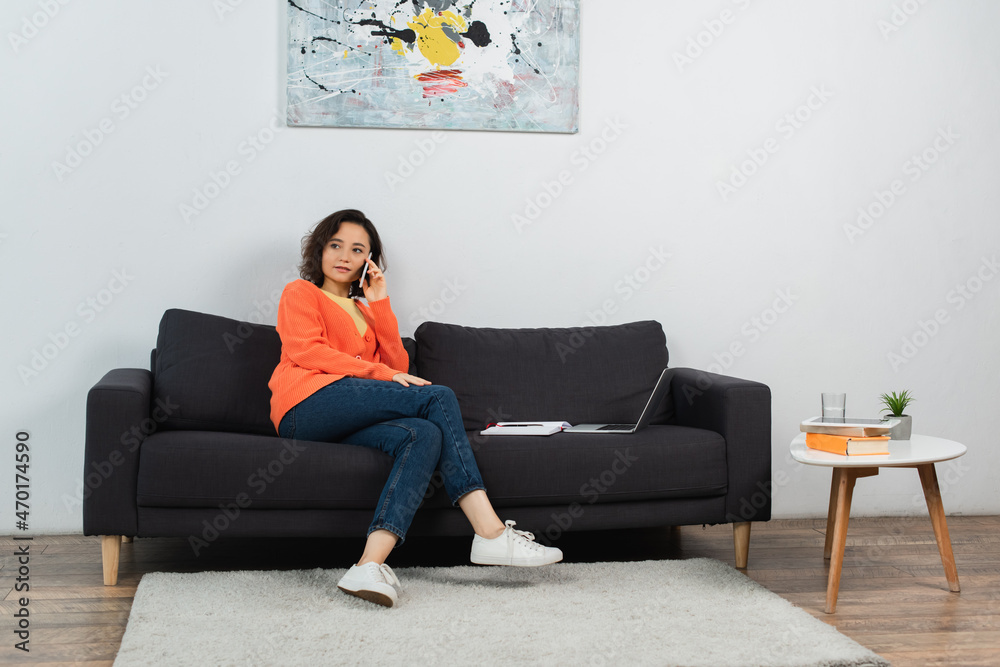 young freelancer talking on smartphone near laptop on couch. young freelancer talking on smartphone near laptop on couch.