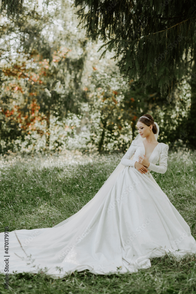 Wonderful bride stands on a tree background in a beautiful white dress