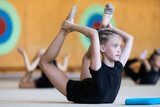 Girl gymnast doing stretching exercise with other trainees on training in gym