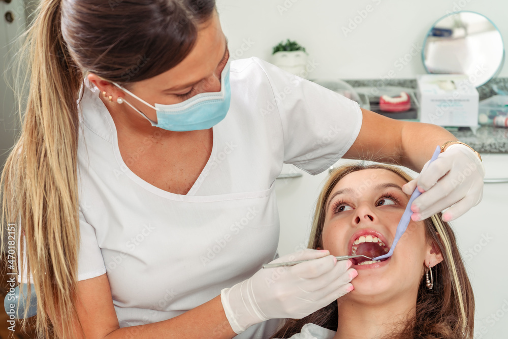 Young female dentist performing a dental cleaning treatment on a young teenage girl. Concept dental care, health care.