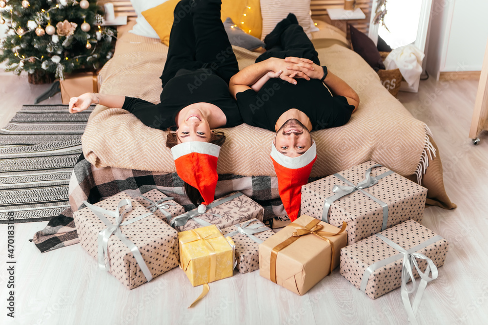 Lovely young romantic couple lying bed near gifts presents garlands home cosy interior atmosphere New Year hat Christmas tree decorations holiday party celebrating concept winter evening 
