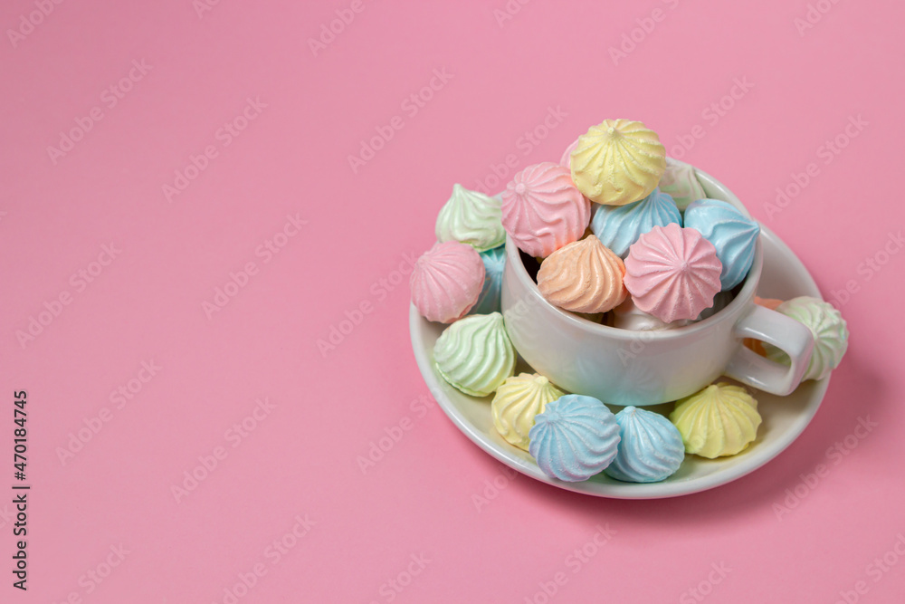 Multicolored meringues on a pink background. A teacup overflowing with colored meringues. Multicolored meringues on a pink background. A teacup overflowing with colored meringues.