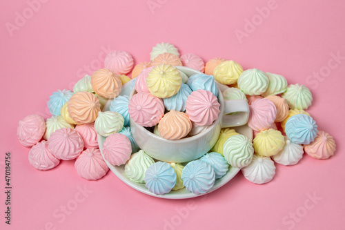 Multicolored meringues on a pink background. A teacup overflowing with colored meringues. © Ruzanna