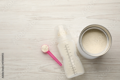 Feeding bottle with infant formula and powder on white wooden table, flat lay. Space for text