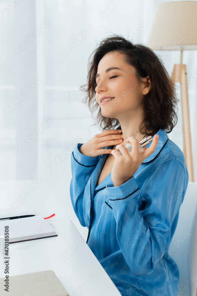 pleased woman spraying perfume on neck.
