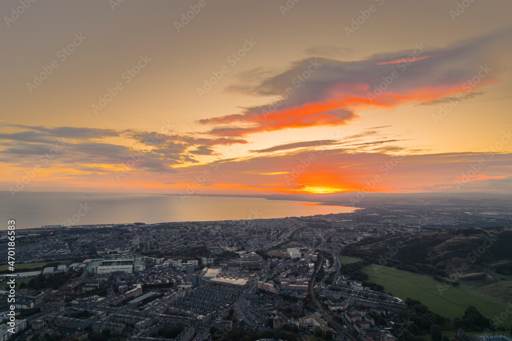 Close-up of the sunrise over city lights of Edinburgh. Aerial view of Edinburgh as the sun rises over the city. Early morning mist creeps along the shoreline of the North Sea like steam from coffee