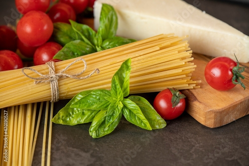 spaghetti on a dark background, cheese, tomatoes, and basil