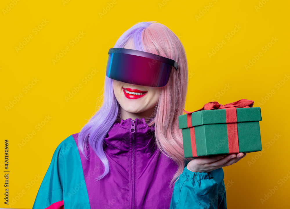 Style woman in VR glasses and 90s sport suit hold gift box on yellow background Style woman in VR glasses and 90s sport suit hold gift box on yellow background