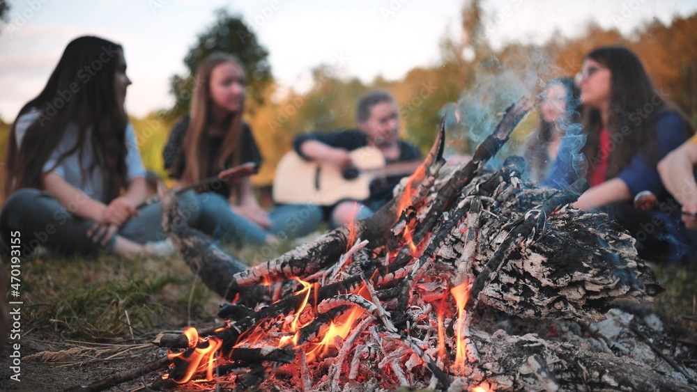 A group of friends with a guitar are sitting around the fire in the evening. A group of friends with a guitar are sitting around the fire in the evening.