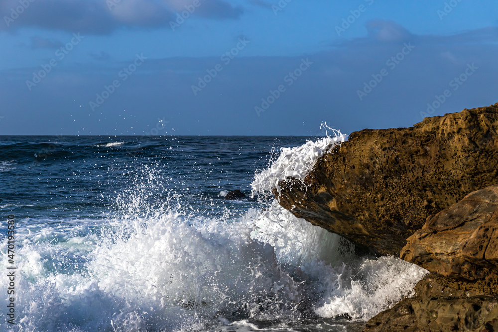 Wave crashing on rock, Southern California Coast, Laguna Nigel. White spray in the air. Pacific ocean, blue sky and clouds behind. 
