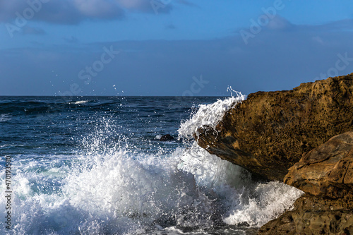 Wave crashing on rock, Southern California Coast, Laguna Nigel. White spray in the air. Pacific ocean, blue sky and clouds behind. 
 photo