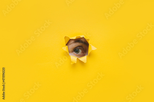 One eye looking through a hole in a yellow paper. Voyeurism. Woman is watching the husband. A curious look. Jealousy, spying on or overhearing the concept. Copy space.