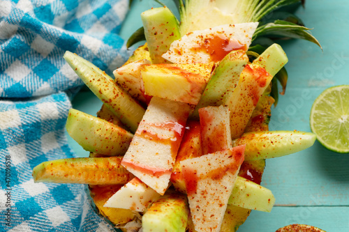 Cucumber, jicama and pineapple with chili powder and chamoy sauce on turquoise background. Mexican snack photo