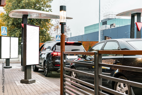 Customers waiting in their cars line up at the drive thru facility of a fast food restaurant. Empty blank vertical banners installed near drive-thru window. Mockup. Mock-up. Poster
