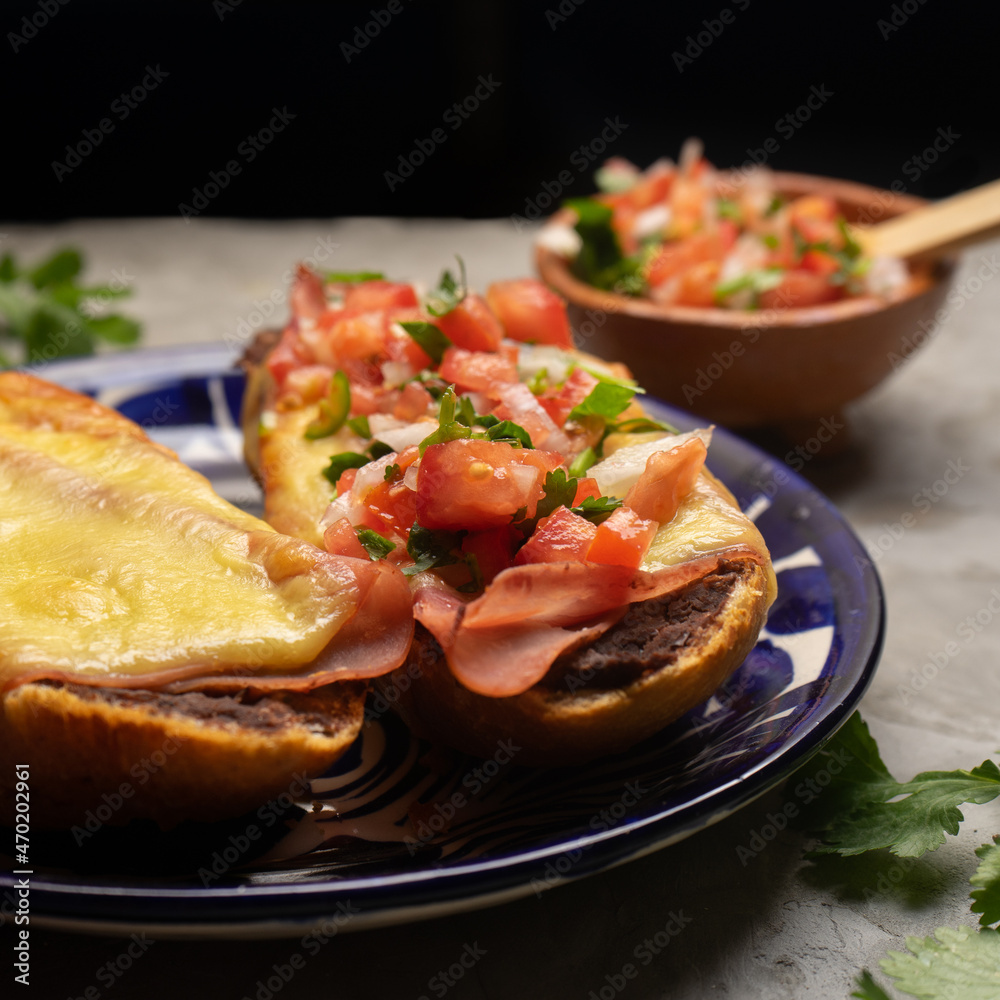 Molletes with ham, refried beans and melted cheese on a gray background. Mexican food