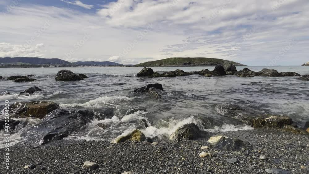 Slow motion view of beautiful, clear ocean water forming small waves and approaching a rocky coast with a black sand beach at low tide. Slow motion view of beautiful, clear ocean water forming small waves and approaching a rocky coast with a black sand beach at low tide.