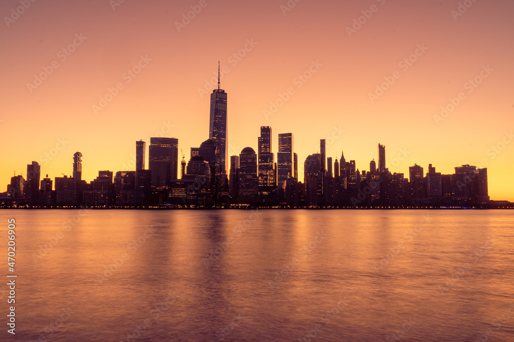 New York, NY - USA -Nov. 14, 2021: Horizontal early morning view of the New York City skyline at sunrise, with golden reflections of the World Trade Center in the Hudson River.