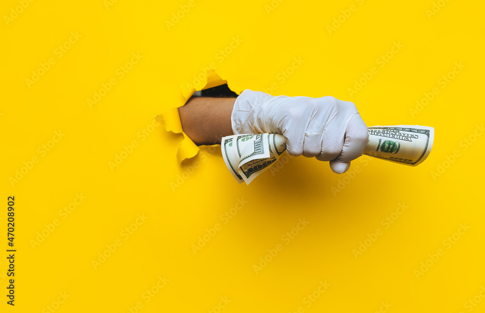 A rifght female doctor holds money in white medical glove. Yellow torn hole paper background.The concept of treatment fees, bribes, illegal surgery. Copy space. A rifght female doctor holds money in white medical glove. Yellow torn hole paper background.The concept of treatment fees, bribes, illegal surgery. Copy space.