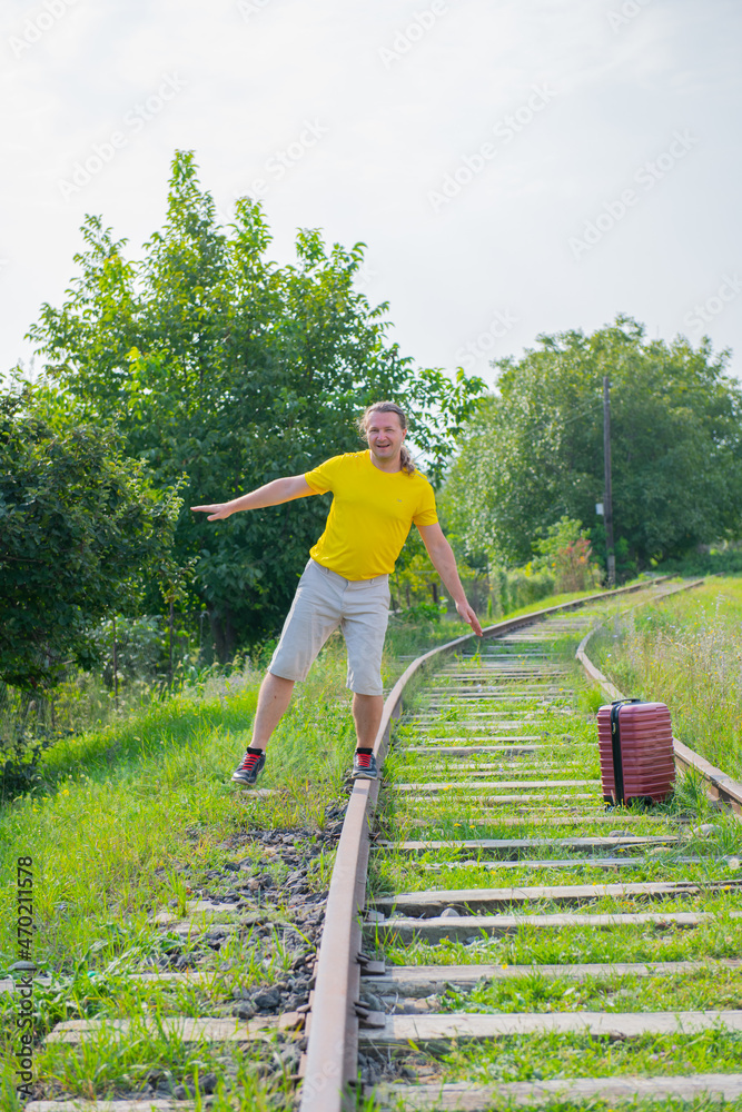 a lone traveler with a red suitcase walks on the rails