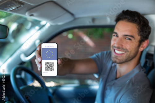 Smiling man in car holding smartphone with covid 19 vaccine passport