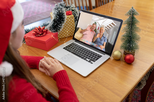 Caucasian woman in santa hat making christmas laptop video call with waving senior couple