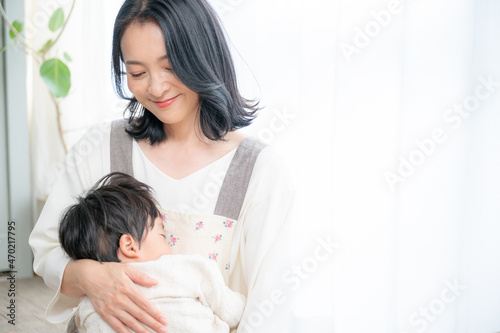 赤ちゃんをリビングで抱っこする笑顔の美人ママ ズーム 右にコピースペース