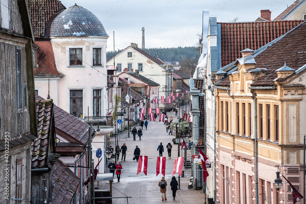 Obraz premium Pedestrian street with people and Latvian red and white flags. Day of proclamation of the Republic of Latvia. Kuldiga, Latvia. Aerial view