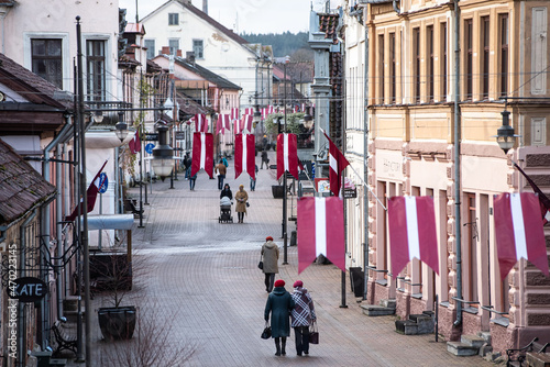 Pedestrian street with people and Latvian red and white flags. Day of proclamation of the Republic of Latvia. Kuldiga, Latvia. Aerial view © Bargais