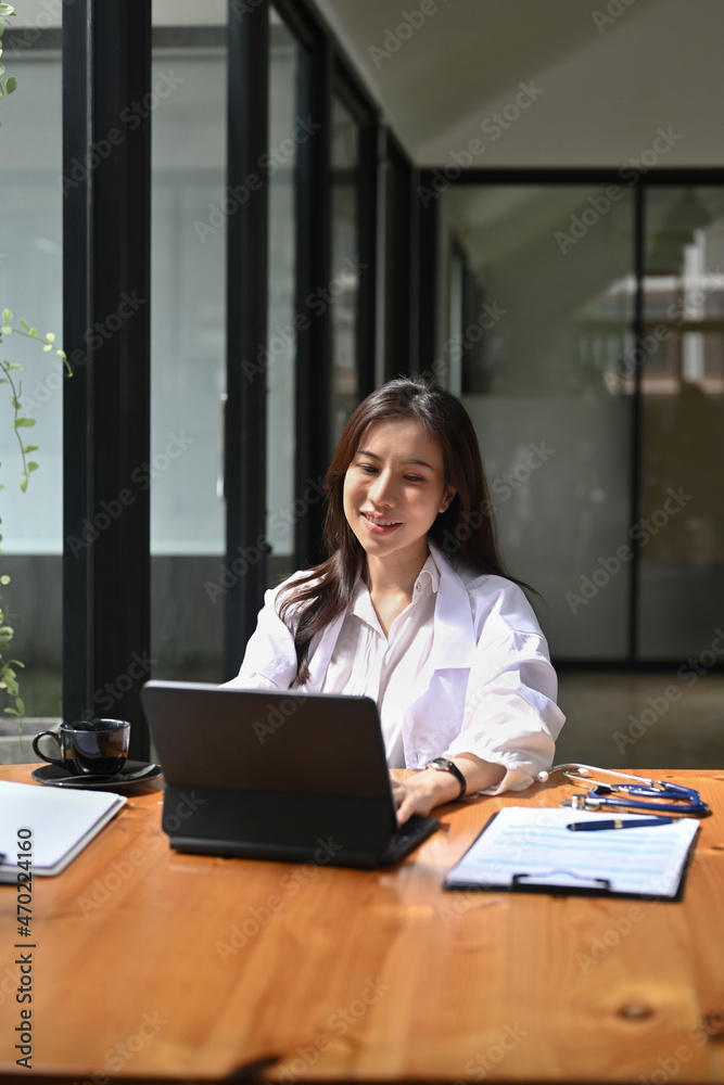 Smiling female doctor in white uniform analyzing patient diagnosis or report in hospital.