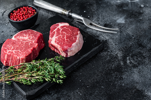 Prime Raw Fillet Mignon tenderloin steaks with thyme. Black background. Top view. Copy space