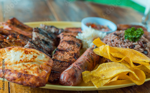 roast beef with rice, fried cheese and tomato salad, Nicaraguan food served on wooden table, plate with assorted types of grilled meats on wooden table photo