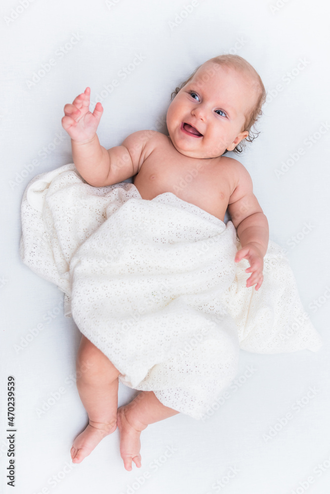 Portrait of a cheerful baby girl who lies on a white sheet and is covered with a woolen cloth Portrait of a cheerful baby girl who lies on a white sheet and is covered with a woolen cloth